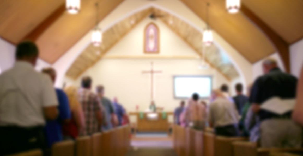 Immagine sfocata di una congregazione di chiesa in piedi davanti a banchi di legno