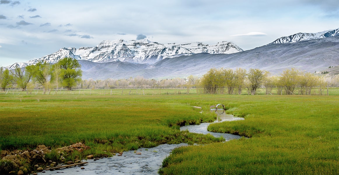Water streaming through a Utah field with snow-capped mountains in the background