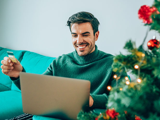 homme assis devant un ordinateur, planifiant et faisant du shopping, entouré de décorations de Noël