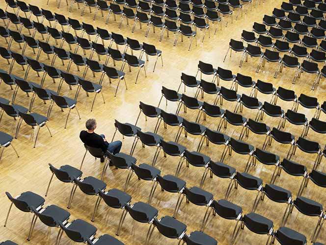 A person sitting alone in a large room filled with rows of plastic chairs