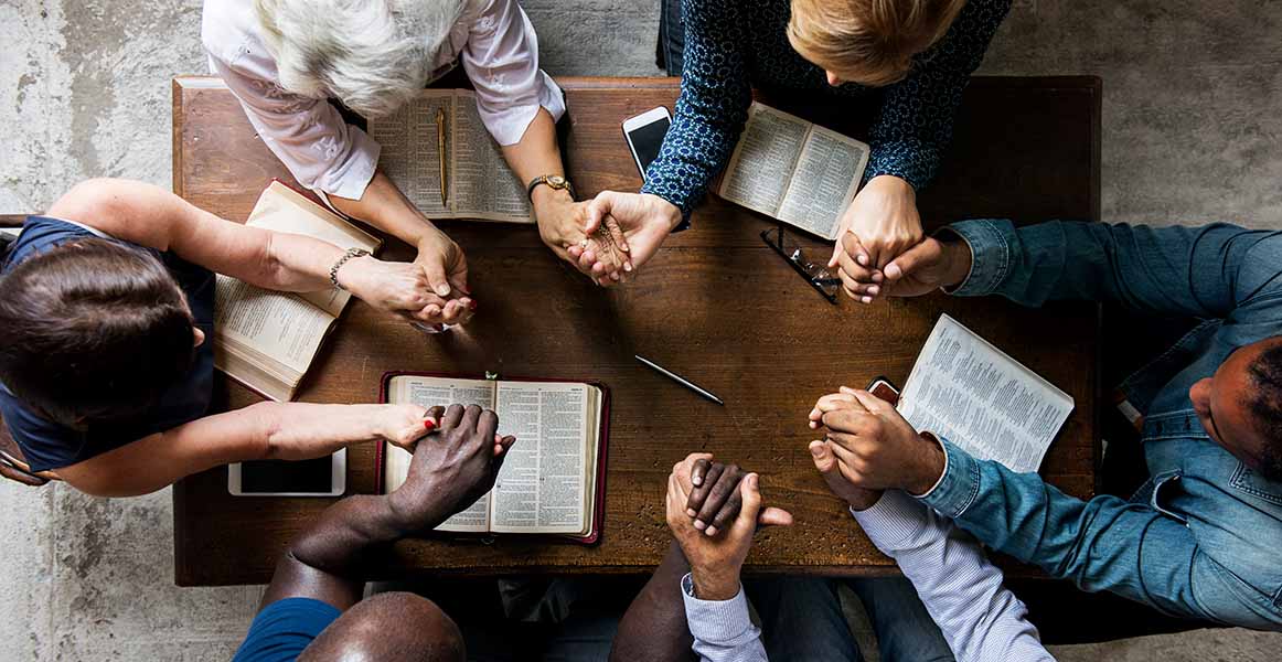 Overhead photo of people at a table with their scripture books and holding hands