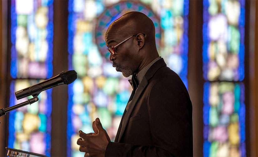 Worship leader speaking at a pulpit with stained glass in the background